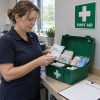 Appointed person using a workplace first aid kit checklist beside an open green kit in a UK workshop office