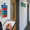 Responsible person reviewing a fire action notice beside an exit route in a UK workplace office